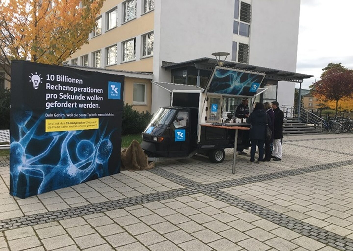 Studierende im Gespräch mit dem Promotion-Team am Kaffeewagen auf dem Campus