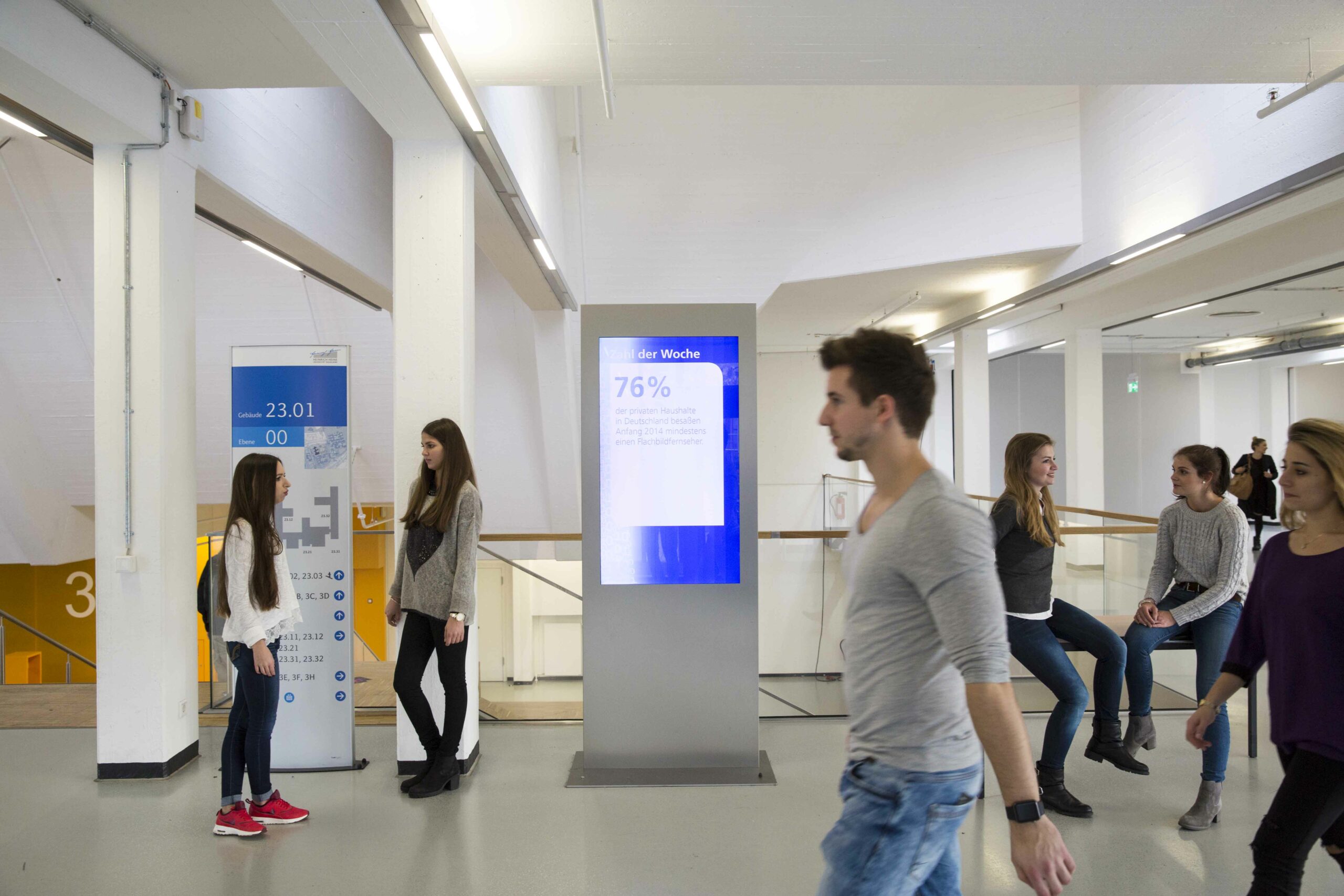 Students pass a digital stele at the University of D&uuml;sseldorf &ndash; DOOH directly on campus for maximum visibility