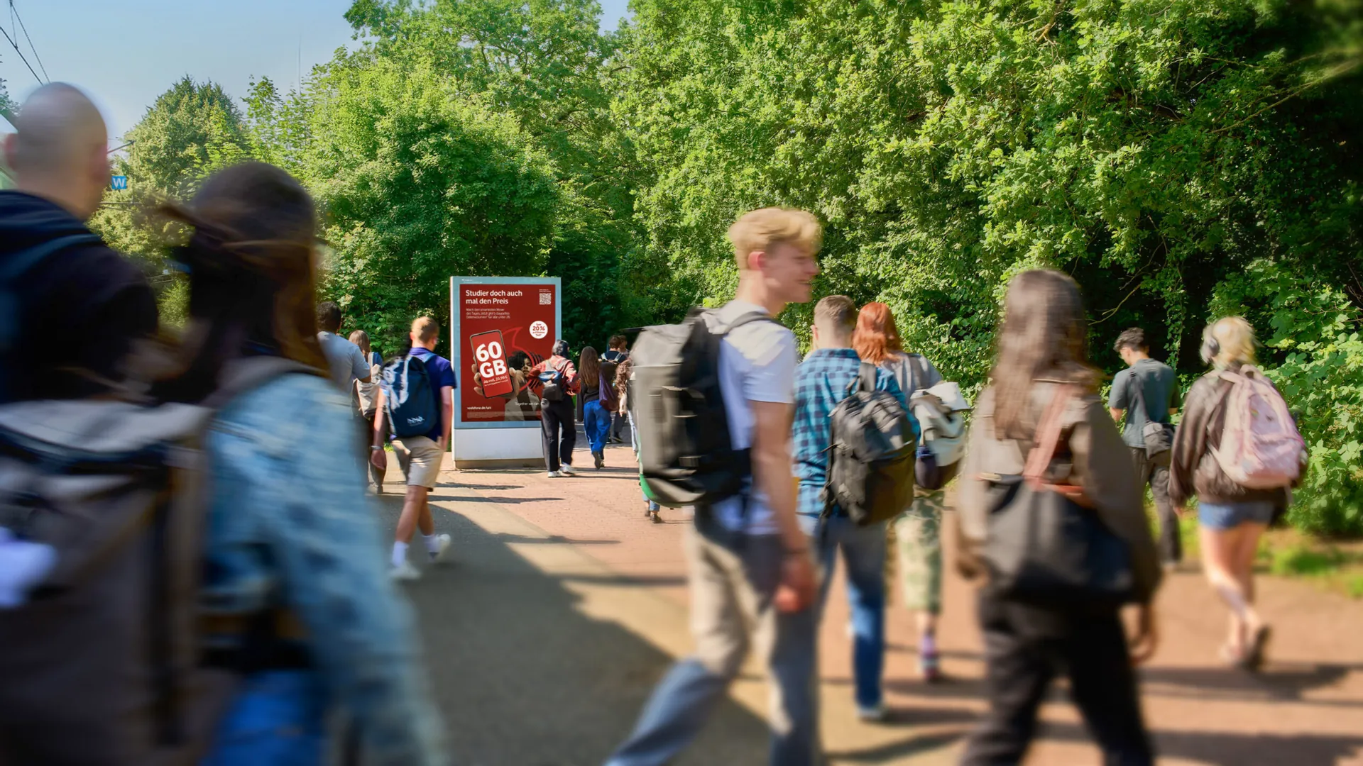 Studierende an der Haltestelle der Heinrich-Heine Universit&auml;t vor einer Plakatwerbung, in diesem Fall einem CLP